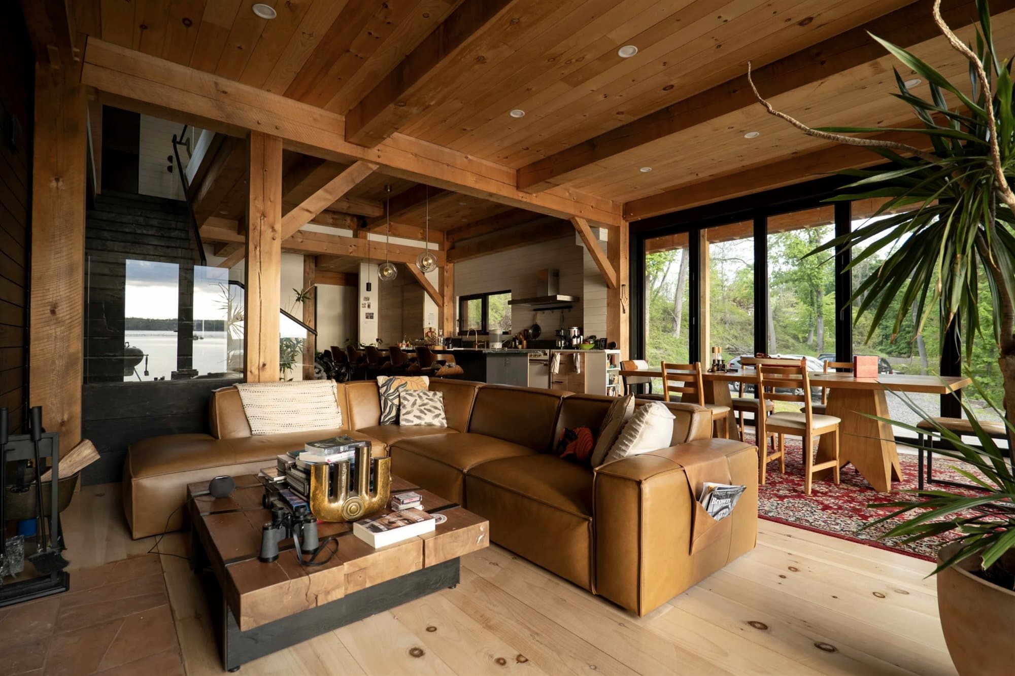 Open-plan great room with exposed timbers, leather seating, kitchen, and dining beyond